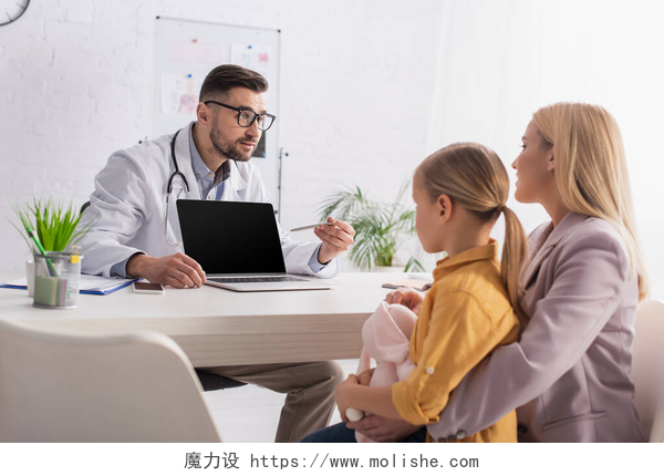 母女在咨询医生问题母亲和女儿看着家庭医生指指点点诊所的笔记本电脑 